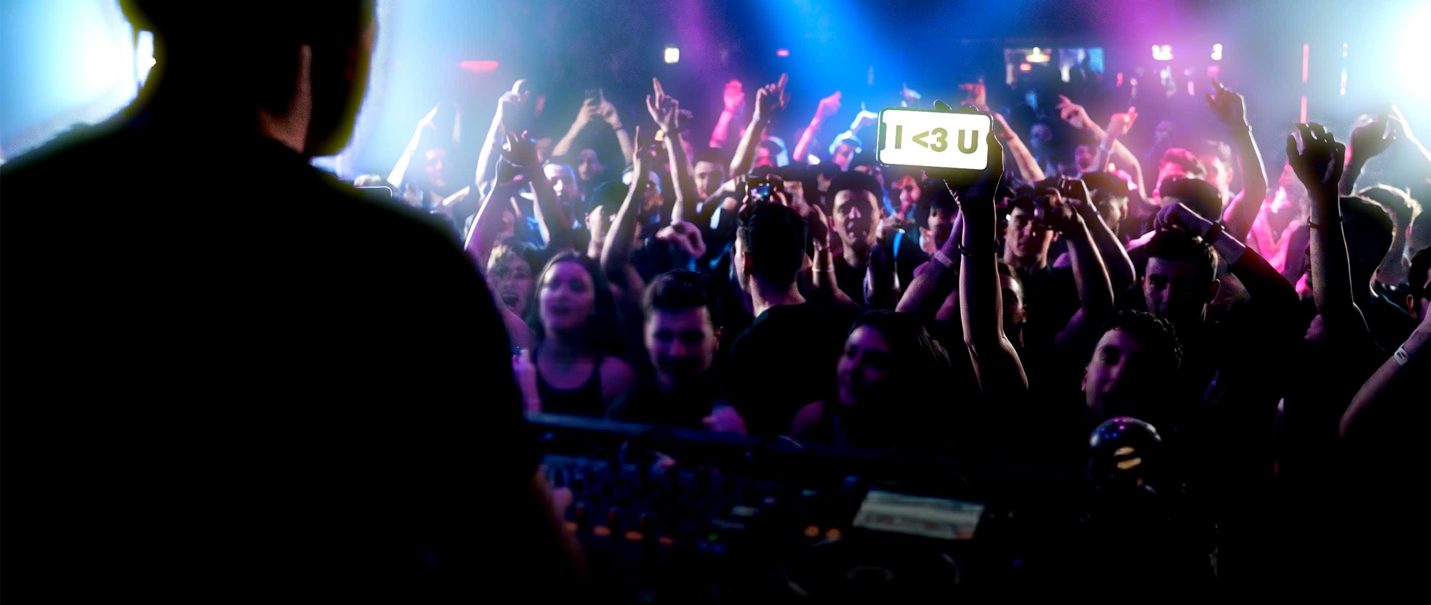Crowd at a concert with raised hands and a stage in the background